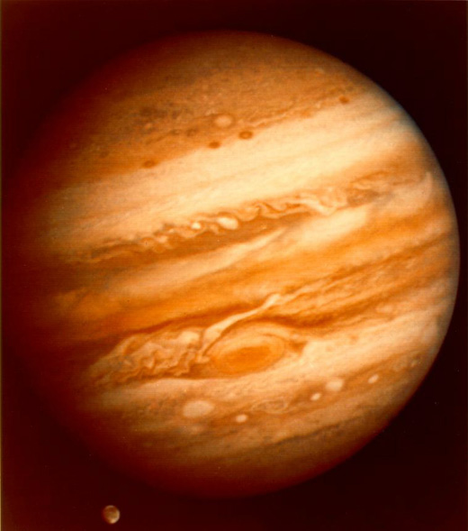 Imagen de Júpiter con su característica distribución en bandas de las masas de gases, y la Mancha Roja en la parte inferior. Por debajo se puede ver a Ganímedes transitando junto al planeta.